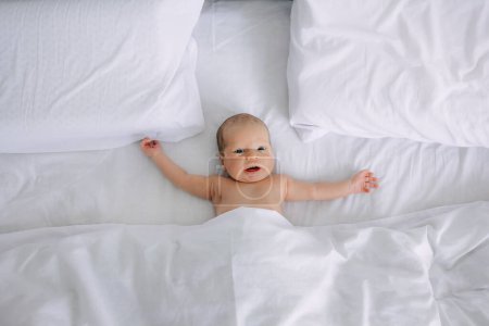 Photo for Top view of adorable baby lying on bed, and looking at camera with curiosity. - Royalty Free Image