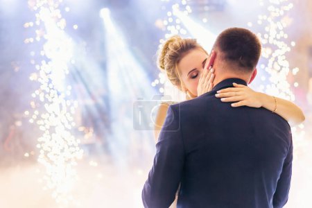 Foto de Los recién casados se abrazan sensualmente mientras bailan en la sala con humo y fuegos artificiales. - Imagen libre de derechos