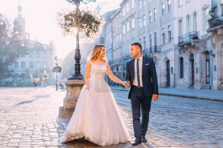 Foto de La novia y el novio se toman de la mano y se miran. paseo por la Plaza de la Ciudad Vieja. - Imagen libre de derechos