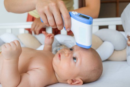 Téléchargez les photos : Femme méconnaissable mesurant la température à un bébé joyeux. Bilan sanitaire - en image libre de droit
