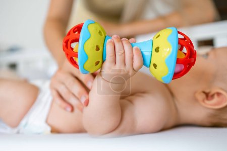 Téléchargez les photos : Bébé tient, joue avec un hochet. Un jouet pour le développement de la motricité fine, des sensations visuelles et auditives. - en image libre de droit