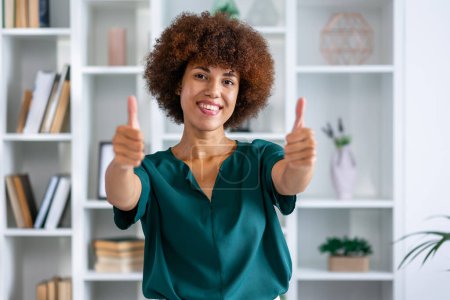 Téléchargez les photos : Jeune heureux plaisir secrétaire employée femme d'affaires en chemise décontractée stand de travail au bureau blanc montrer pouces geste - en image libre de droit