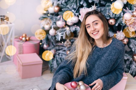 Photo for Cute girl sitting against the Christmas tree and holding the box with gifts. close up. - Royalty Free Image
