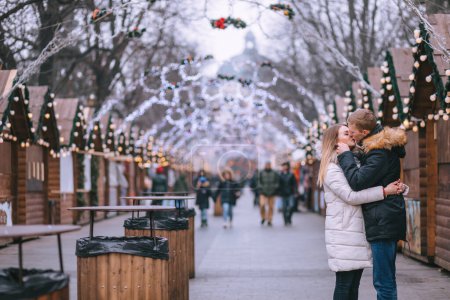 Téléchargez les photos : Joyeux couple en vêtements chauds, embrassant, posant au marché de Noël. Humeur festive. - en image libre de droit