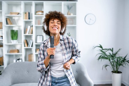 Photo for Music Lover Concept. Overjoyed african american lady wearing wireless headphones listening to favourite song, dancing at home with closed eyes. Female taking break, copy space - Royalty Free Image