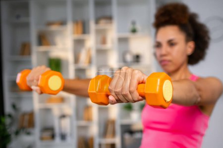 Photo for Dumbbells selective focus in hand of athletic girl at home. Sport, healthy lifestyle. - Royalty Free Image