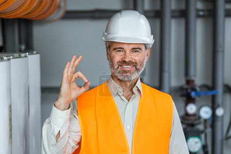 Photo for Portrait of technician standing inside heating plant boiler department showing ok sign - Royalty Free Image