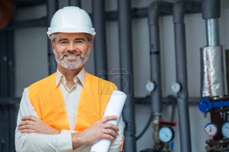 Foto de Senior gris pelo feliz sonriente ingeniero profesional trabajador vistiendo uniforme, y sombrero duro en sala de calderas. - Imagen libre de derechos