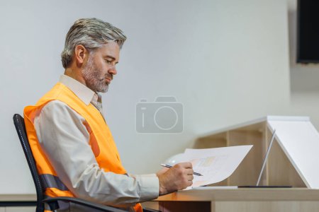 Photo for Competent mature senior gray haired architect male sitting on desk indoors doing project drawings. - Royalty Free Image