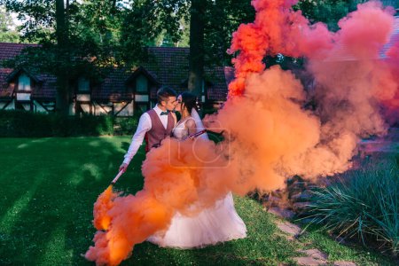 Foto de Hermosos recién casados se paran en el bosque y sostienen coloridas bombas de humo en sus manos. Fotografía de boda. - Imagen libre de derechos