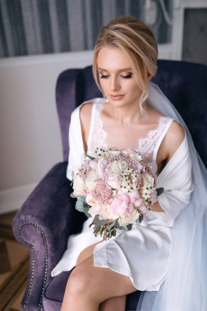 Téléchargez les photos : La mariée blonde est assise dans un fauteuil luxueux avec un bouquet - en image libre de droit