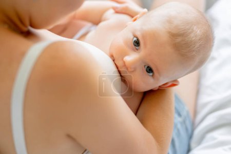 Photo for Peaceful loving young mother sitting on bed feeding baby with breast - Royalty Free Image