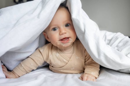 Téléchargez les photos : Bébé garçon se cache sous la couverture blanche - en image libre de droit