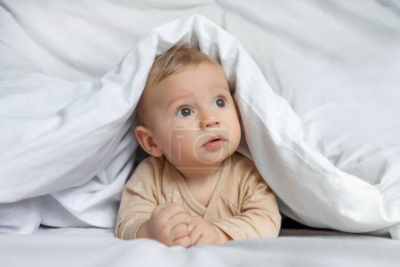Photo for Cute little baby playing hiding under white blanket at home. - Royalty Free Image