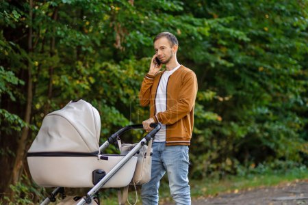 Photo for Man talking on mobile phone and pushing stroller outdoors. Father on paternity leave. - Royalty Free Image