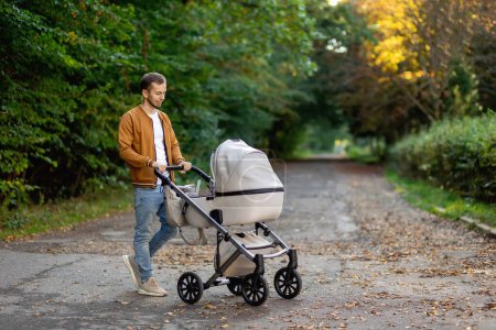 Photo for A young father walks with a stroller in the park. Walk with the child in the fresh air. - Royalty Free Image