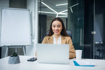 Téléchargez les photos : Portrait d'une femme d'affaires joyeuse assise à la table au bureau regarder le travail de l'ordinateur portable sur le projet - en image libre de droit