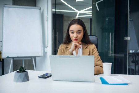 Téléchargez les photos : Une femme d'affaires attrayante assise devant un ordinateur portable et gérant son entreprise depuis son bureau. - en image libre de droit
