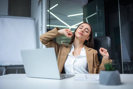Téléchargez les photos : Femme de bureau détendue étirant les mains et le corps prenant une pause du travail sur ordinateur portable. Joyeuse rédactrice pigiste heureuse de la tâche effectuée sur le lieu de travail dans l'espace de coworking - en image libre de droit