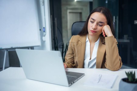 agotada mujer de negocios sintiéndose cansado y tratando de concentrarse en la pantalla de la computadora portátil en el gabinete hacen tarea poco interesante.