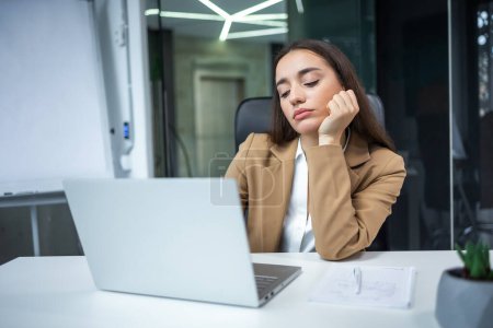 Photo for Young woman dressed in shirt sitting at her workplace at the office, looking bored at laptop computer - Royalty Free Image