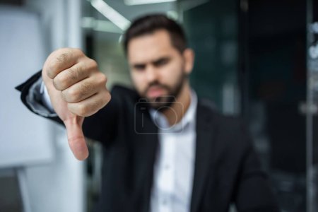 Foto de Hombre de negocios Mostrar signo de fracaso. Un hombre de negocios con problemas en los negocios muestra su pulgar en la oficina. - Imagen libre de derechos