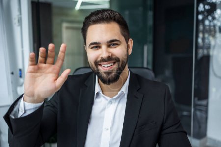 Portrait of smiling male Caucasian boss sit at office desk greeting look at camera in modern office, happy man worker millennial businessman posing, having video call with client or customer online