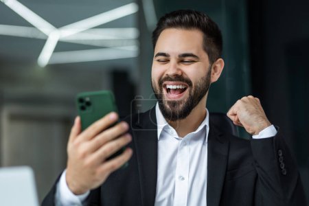 Photo for Excited man sit at desk triumph win online lottery on cellphone, overjoyed businessman feel euphoric read good unexpected news or message on smartphone - Royalty Free Image