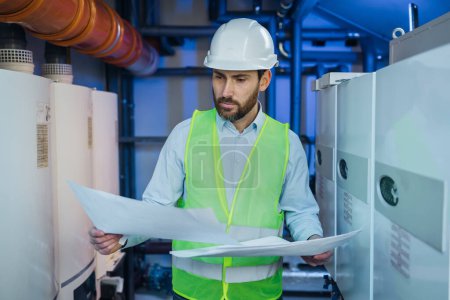 Focused engineer standing near heating system and checking correspondence of data with construction drawing.