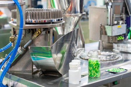 Photo for Close up green capsule in transparent and white plastic bottle place on automatic capsule filling machine for medical industrial - Royalty Free Image