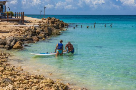 Photo for Beautiful view of couple fixing surfboard in water on coastline. Aruba. Oranjestad. 09.09.2022. - Royalty Free Image