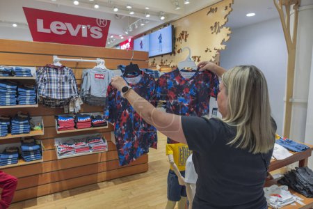 Téléchargez les photos : Woman choose T-shirt in children's department for shop Macy's supermarket. New York. USA. 09.21.2022. - en image libre de droit