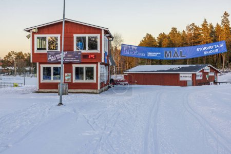 Foto de View at building of ski sport club on forest trees and pale sky background. Sweden. Storvreta. 02.26.2023. - Imagen libre de derechos