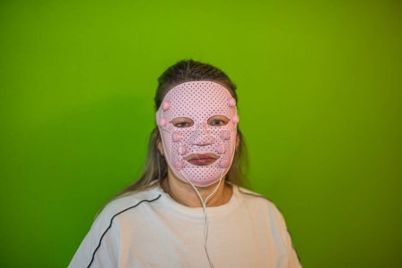 Photo for Close-up view of woman with pink face massager mask on green background. Sweden. - Royalty Free Image