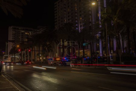 Photo for Night view of Miami Beach cityscape with police cars and defocused light tracers of cars on Collins Avenue. Miami Beach. USA - Royalty Free Image