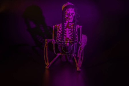 Foto de Vista de cerca del esqueleto iluminado rosa sentado con las piernas dobladas sobre fondo negro. Concepto de Halloween. Países Bajos. - Imagen libre de derechos