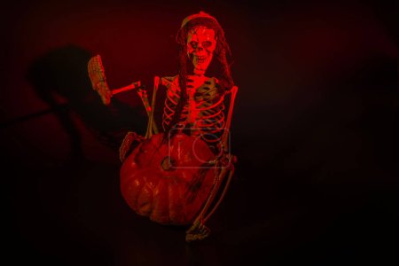 Foto de Vista de cerca del esqueleto iluminado en rojo sentado junto a la calabaza de Halloween. Países Bajos. - Imagen libre de derechos