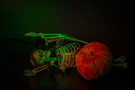 Foto de Figura esqueleto de juguete junto a calabaza naranja sobre fondo negro. concepto de decoración de Halloween. - Imagen libre de derechos