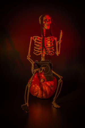 Foto de Vista de cerca del esqueleto sentado en calabaza para Halloween con luz de fondo roja sobre fondo negro. Países Bajos. - Imagen libre de derechos