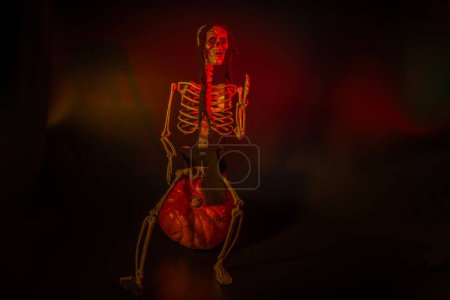 Foto de Vista del esqueleto sentado en calabaza para Halloween con luz de fondo naranja sobre fondo negro. Países Bajos. - Imagen libre de derechos
