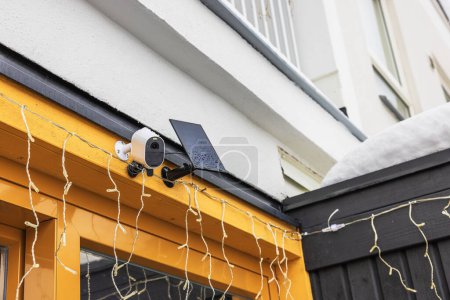 Nahaufnahme der Außen-Überwachungskamera mit Solarpaneel an der Fassade der Villa an frostigen Wintertagen installiert. Schweden.