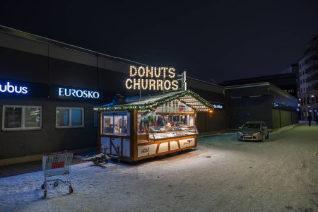 Foto de Vista de cerca de un quiosco de la calle que vende donas y churros iluminados en una noche de invierno. - Imagen libre de derechos