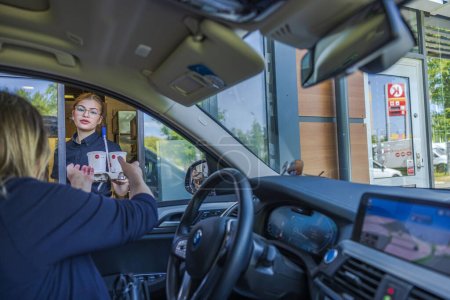 Téléchargez les photos : Une conductrice recevant une commande complétée d'un employé de McDonald's par la fenêtre de conduite. - en image libre de droit