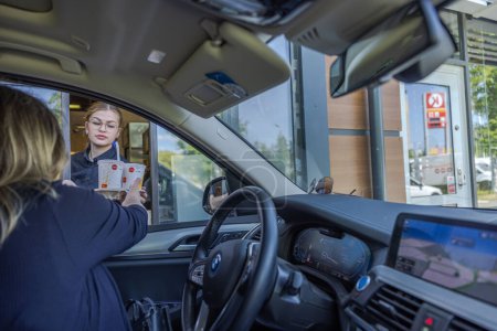 Photo for Close up view of woman driver receiving completed order from McDonald's employee at drive-in window. - Royalty Free Image