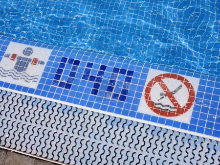 Téléchargez les photos : Une vue sur le bord de la piscine avec une profondeur spécifiée pour la baignade en toute sécurité et un panneau d'avertissement interdisant la plongée. Espagne. - en image libre de droit