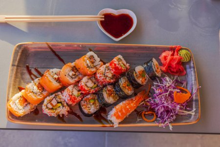 Photo for Beautiful view of plate with diverse sushi, sauce, and wooden chopsticks on table in restaurant. Curacao. - Royalty Free Image