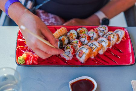 Photo for Close-up of female hands picking up sushi with chopsticks from plate. Curacao. - Royalty Free Image