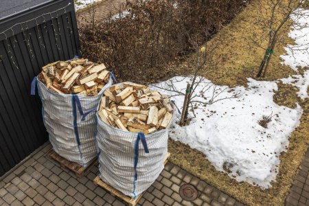 Close-up top view of spring garden with transport bags of chopped birch firewood near house. Sweden.