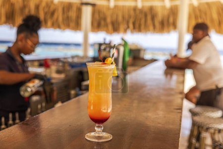 Photo for Close up view of a glass of orange-toned cocktail on the bar counter of an outdoor hotel restaurant located on the coastline. Curacao. - Royalty Free Image