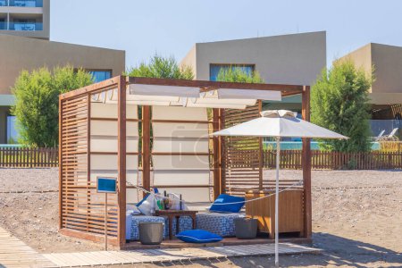 Close up view of personal wooden covered cabana on the sandy beach of the hotel with a sun lounger, a sunshade, and a table for beverages. Rhodes. Greece.